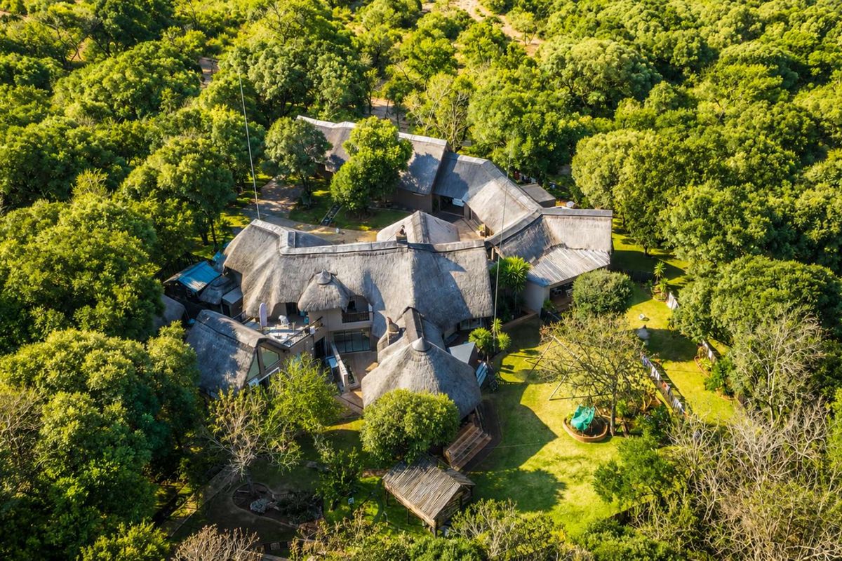 Aerial view of a large property featuring a traditional thatched roof design, surrounded by extensive mature trees and landscaped garden areas.