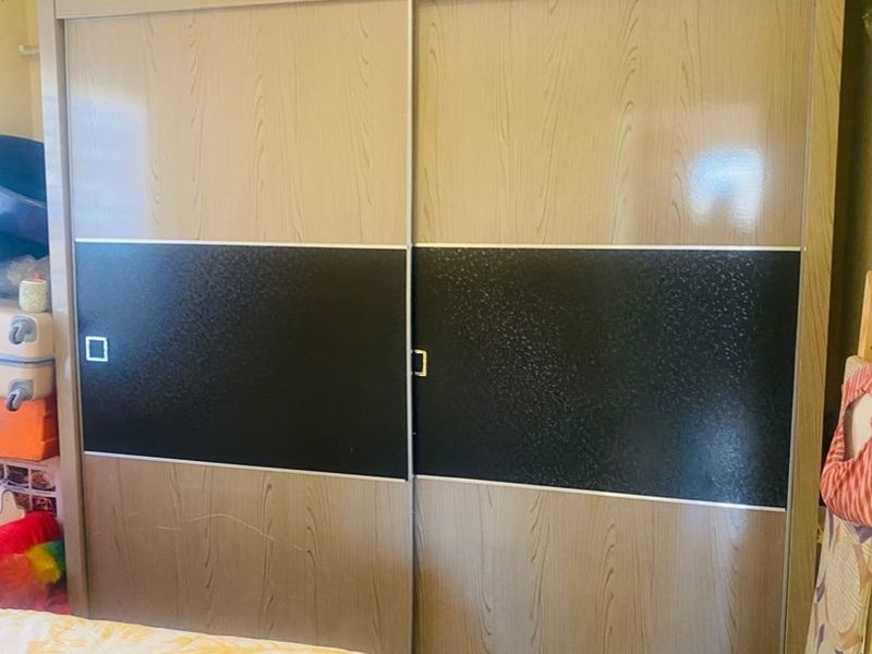 A bedroom featuring a large, modern built-in sliding door wardrobe with a two-tone wood and black finish.