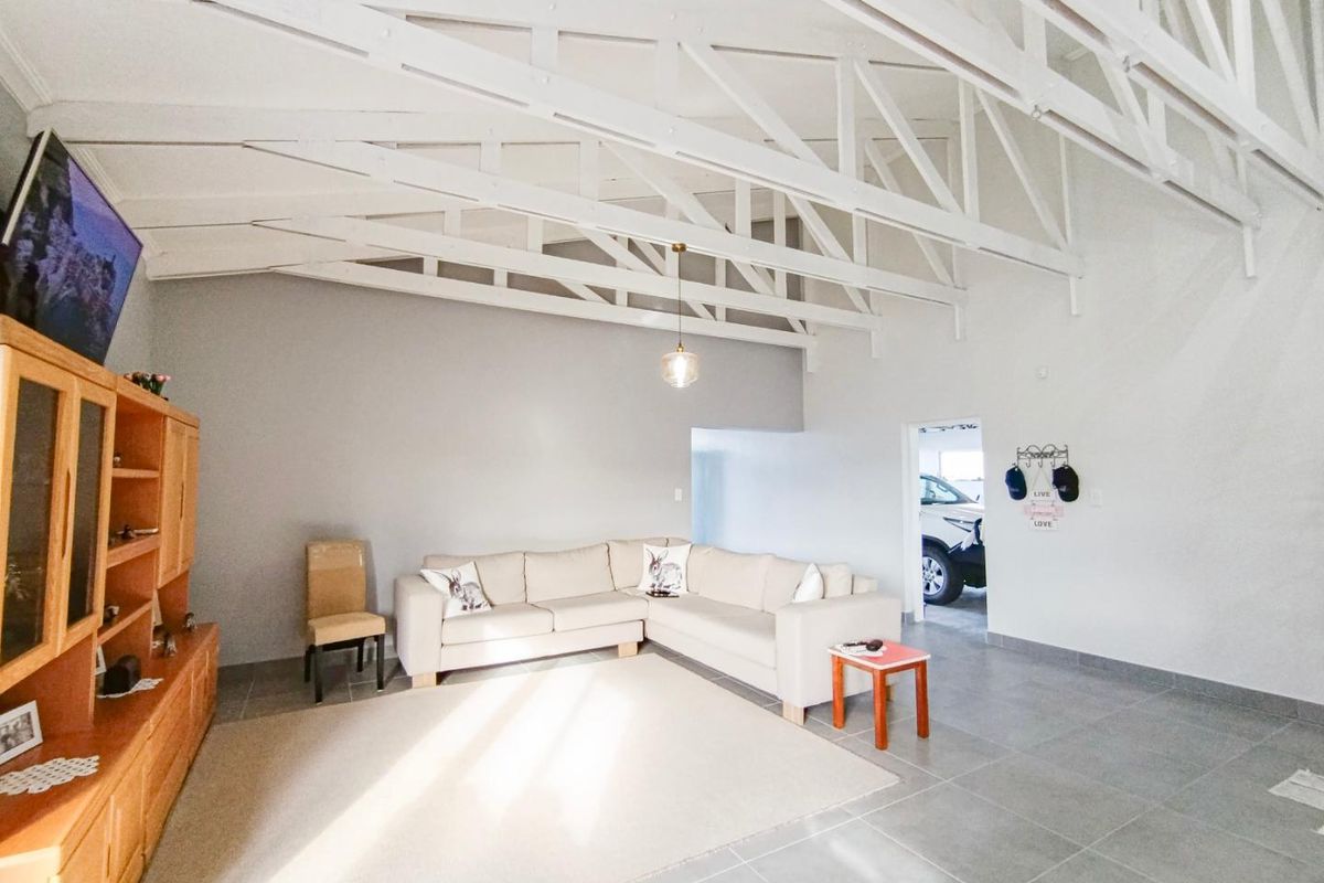 Spacious living area featuring high vaulted ceilings with exposed white trusses and neutral tiled flooring.