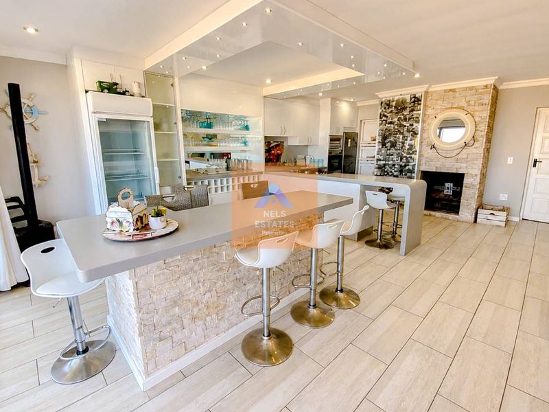 Spacious open-plan living and kitchen area featuring a stone-clad breakfast bar, built-in fireplace, and modern recessed ceiling lighting with tiled flooring throughout.