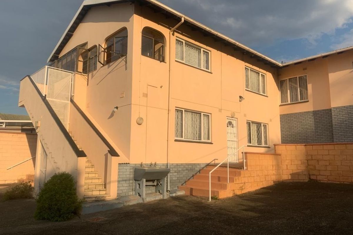 Rear exterior view of a multi-level residential building featuring an external staircase, paved courtyard area, and functional utility sink.