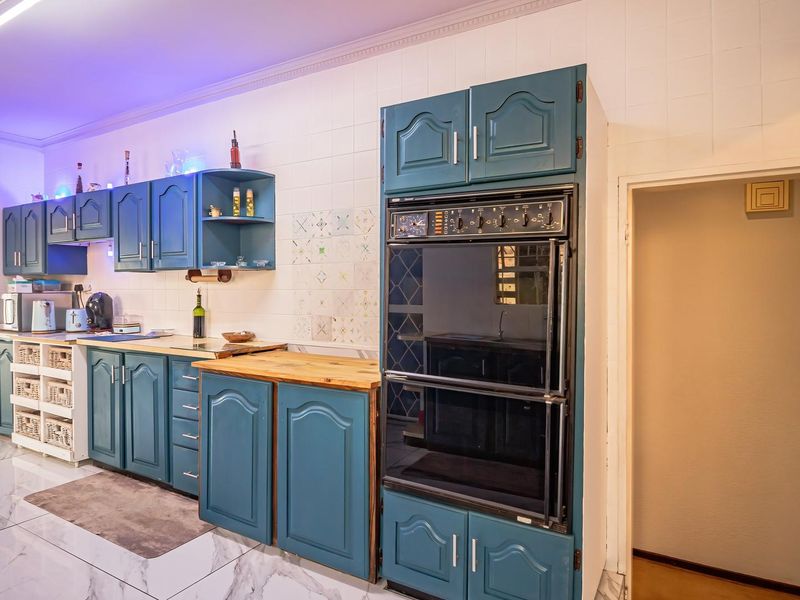 A functional kitchen featuring blue cabinetry, a double wall oven, tiled backsplash, and marble-look flooring, offering a solid foundation for a modern update.