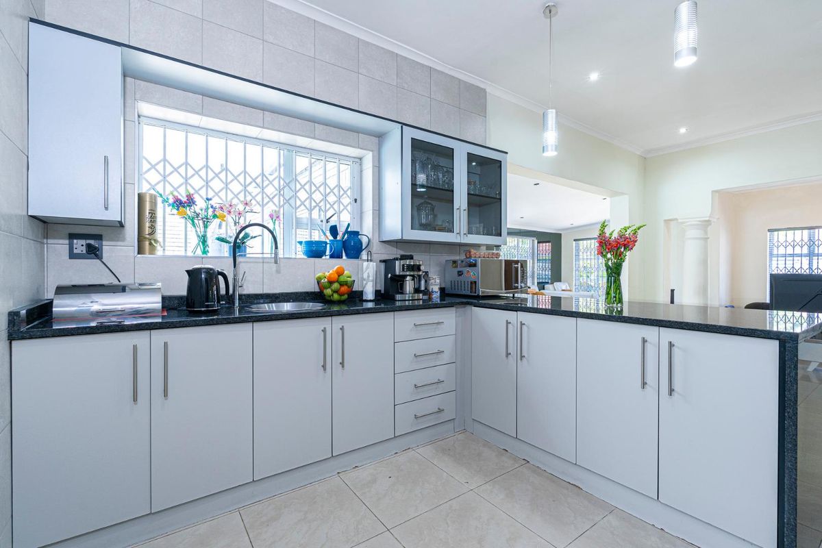 Modern kitchen featuring light grey cabinetry, dark granite countertops, tiled splashbacks, and a stainless steel sink with a view through the window.