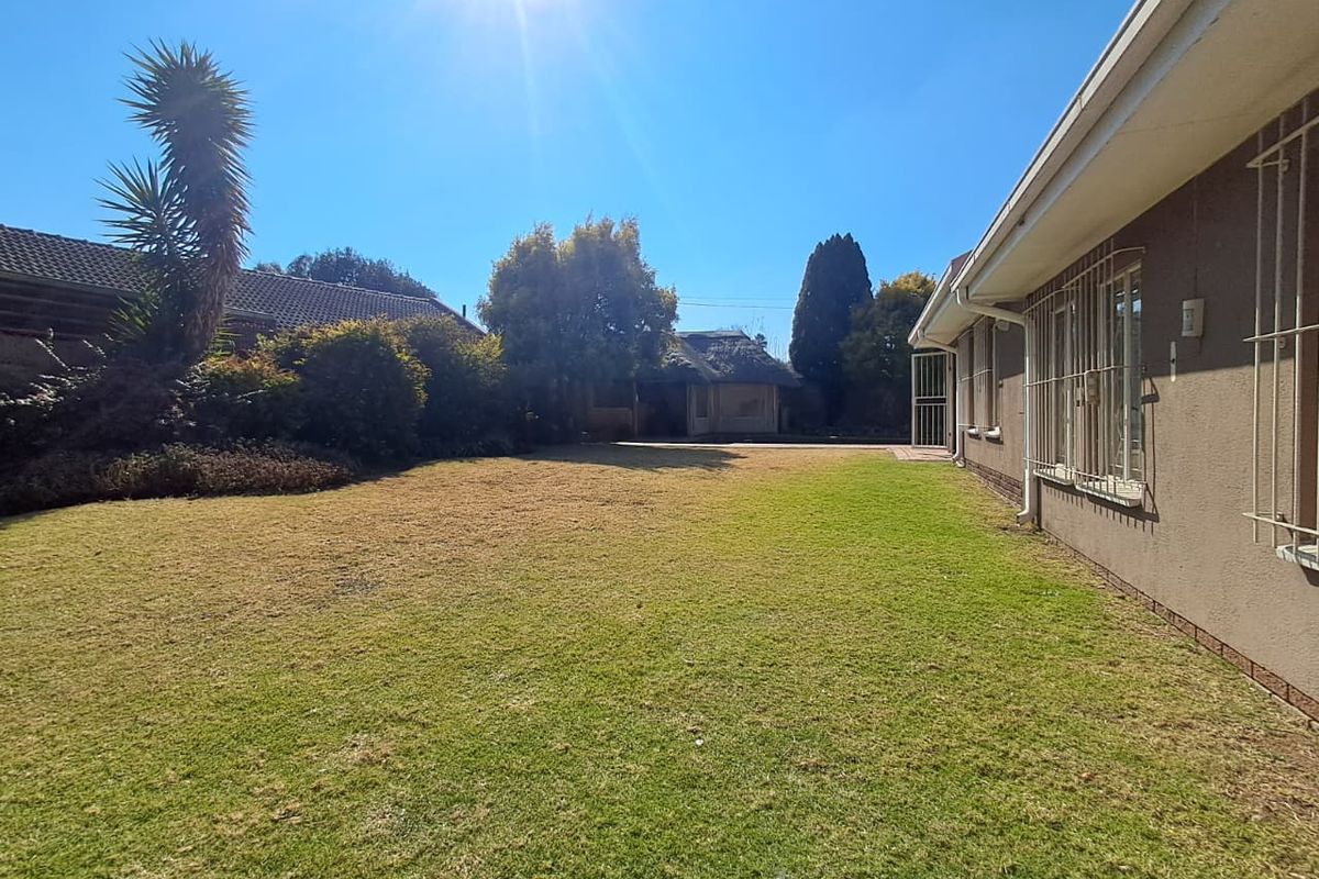 A spacious rear garden featuring a well-maintained lawn area adjacent to the side of the house with installed security bars on windows.