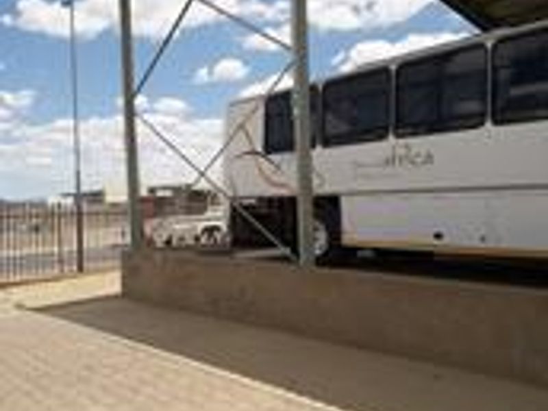 Industrial outdoor covered parking area featuring a steel frame structure with corrugated metal roofing and paved ground surface.