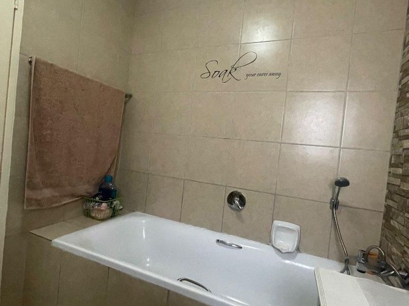 A functional bathroom featuring a built-in bathtub with a handheld shower attachment, neutral wall tiling, and a decorative stone-cladding accent wall.