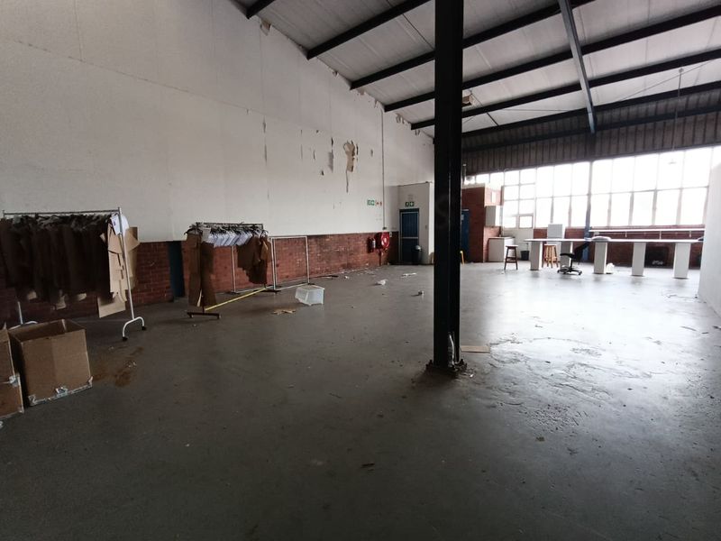 Spacious industrial utility area featuring high ceilings with exposed steel trusses, concrete flooring, and large windows providing ample natural light.