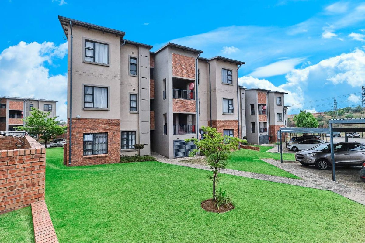 Exterior view of a multi-story townhouse complex featuring brick and plaster facade, paved walkways, and communal garden areas with covered parking bays.