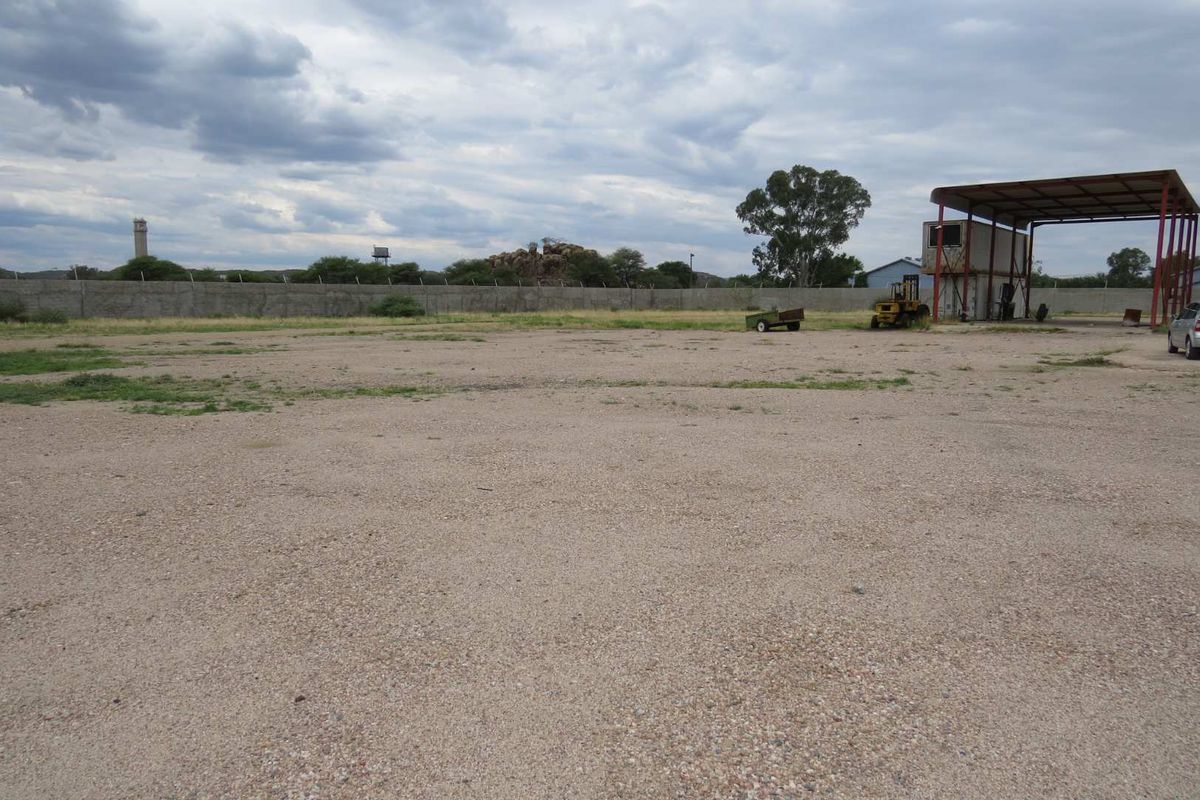 Expansive industrial yard featuring a gravel surface, perimeter wall, and a large covered steel structure for outdoor storage or operations.