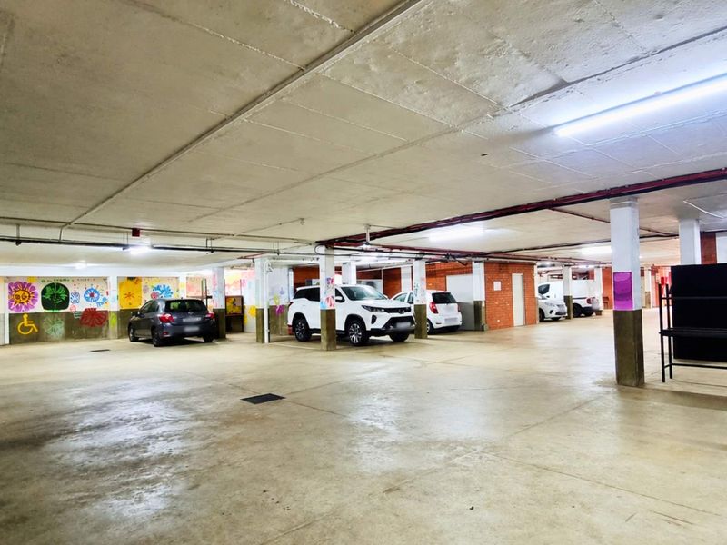 A spacious underground parking garage featuring concrete flooring, structural columns, and overhead fluorescent lighting, providing ample covered parking space.