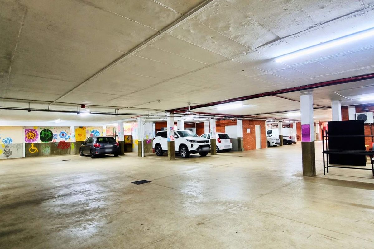 A spacious underground parking garage featuring concrete flooring, structural columns, and overhead fluorescent lighting, providing ample covered parking space.