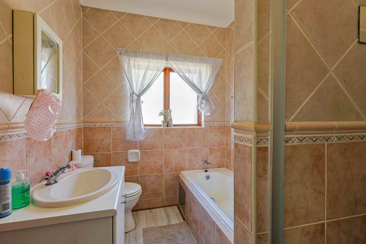 A functional bathroom featuring a built-in bathtub, vanity basin, and toilet, finished with classic ceramic wall tiles and a window for natural light.