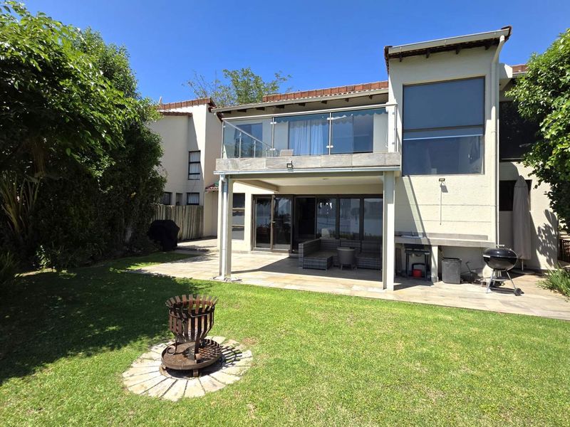 Rear view of the townhouse featuring a landscaped garden, a covered patio area with a built-in counter, and an upper-level balcony with glass balustrades.