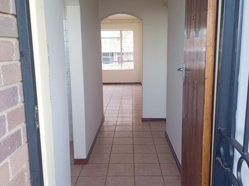 A clean, tiled hallway featuring arched architectural details, leading from an entrance with a security gate into the main living area.