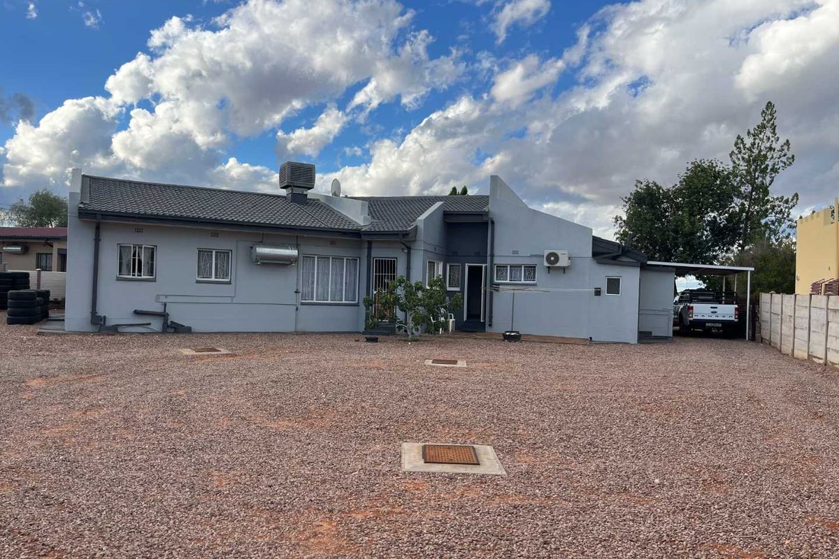 Rear view of the property featuring a gravel yard, tiled roof, evaporative cooler, and a covered carport area.
