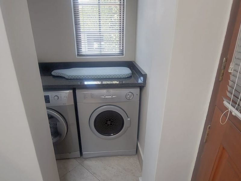 A compact, functional laundry nook featuring granite countertops, tiled flooring, and built-in space for laundry appliances.