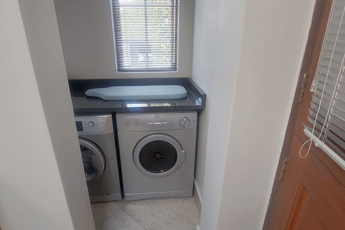 A compact, functional laundry nook featuring granite countertops, tiled flooring, and built-in space for laundry appliances.