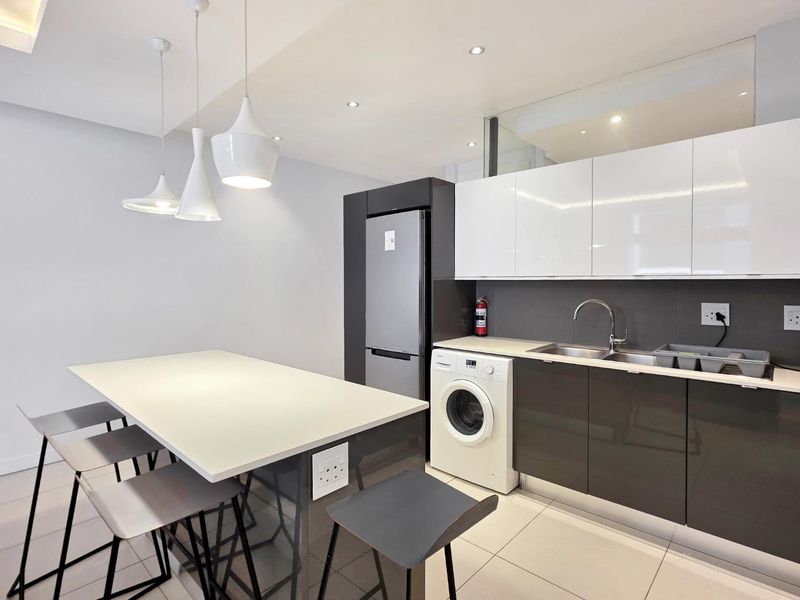 Modern kitchen featuring sleek high-gloss cabinetry, a central island with breakfast bar seating, integrated laundry appliances, and contemporary pendant lighting.