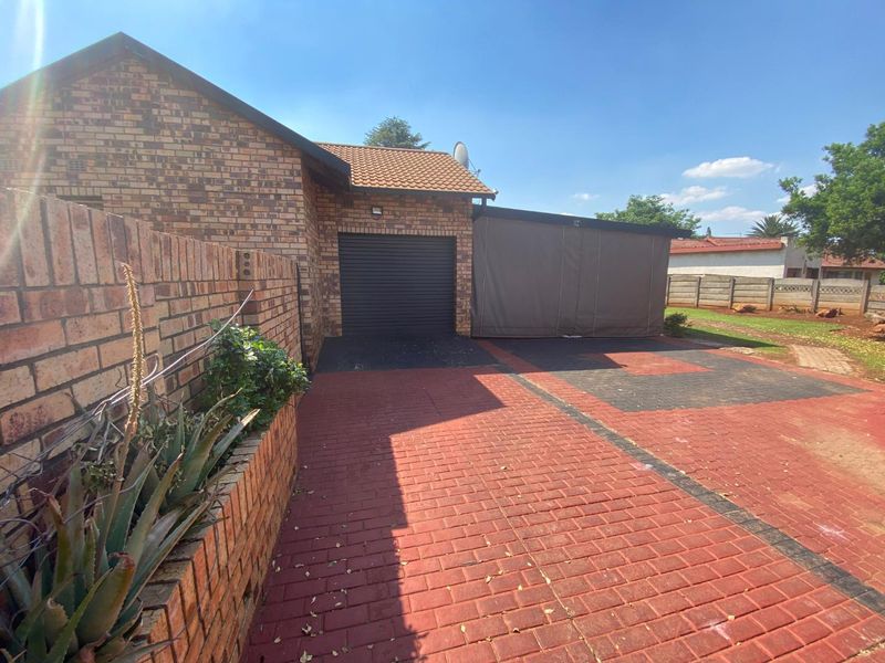 Front exterior view of the property featuring a face brick facade, single garage, paved driveway, and a covered carport area.