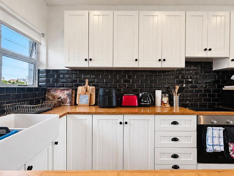 A well-maintained kitchen featuring white shaker-style cabinetry, a contrasting black subway tile backsplash, butcher block countertops, and a classic farmhouse sink.