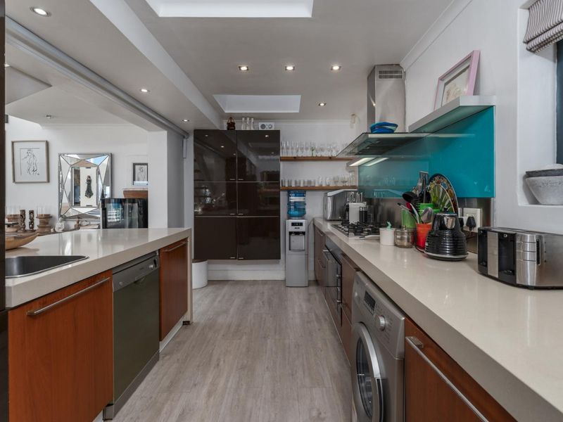 Modern galley-style kitchen featuring stone countertops, integrated appliances, gas hob, extractor fan, and a bright skylight, seamlessly flowing into the adjacent living area.