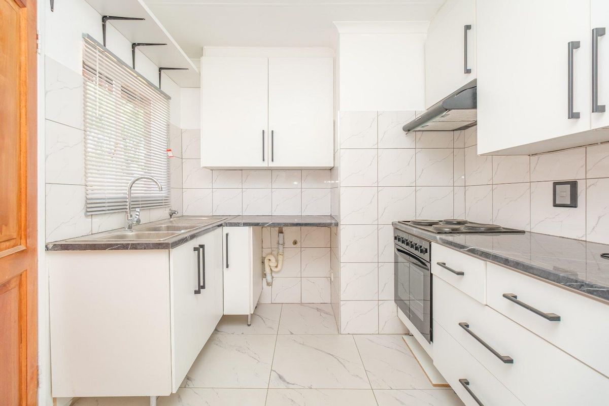 A clean, functional kitchen featuring white cabinetry, dark laminate countertops, tiled splashbacks, and integrated cooking appliances.