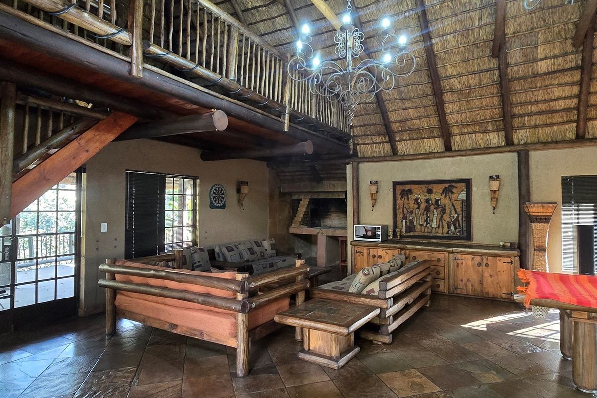 Spacious living area featuring a high thatched ceiling, exposed timber beams, a mezzanine level, and a built-in fireplace with stone tile flooring.