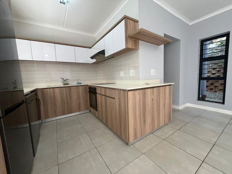 Modern kitchen featuring wood-grain and white cabinetry, stone countertops, integrated oven, cooktop, extractor fan, and neutral tiled flooring.