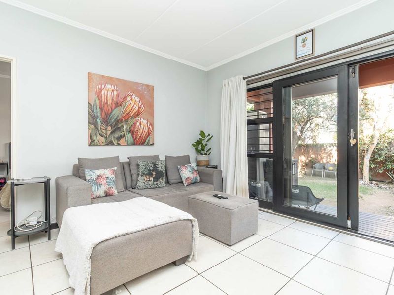 A bright living room featuring tiled flooring and a large sliding glass door providing direct access to the outdoor patio and garden area.