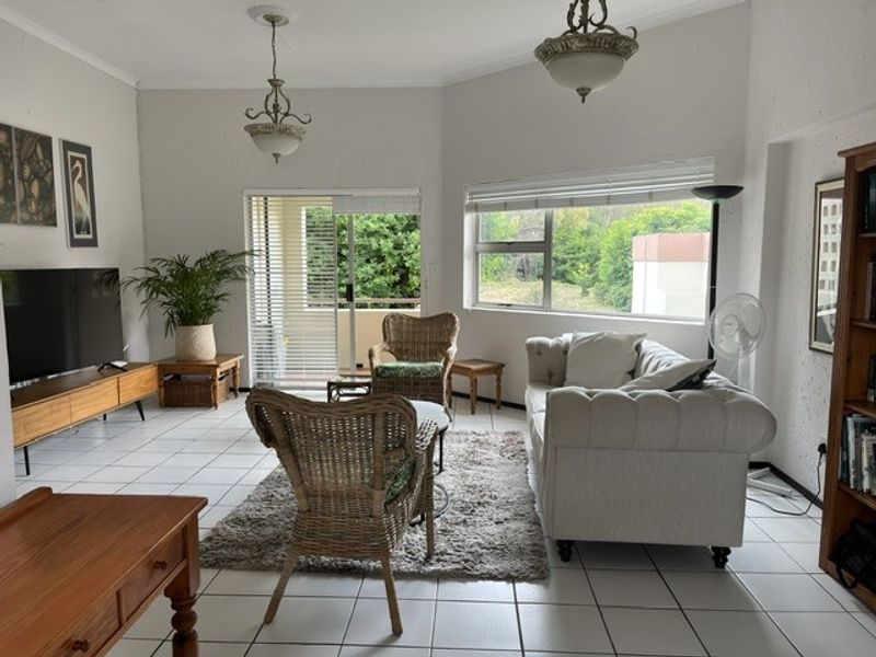 Spacious living room featuring tiled flooring, large windows, and a sliding glass door leading to an outdoor area, providing ample natural light.