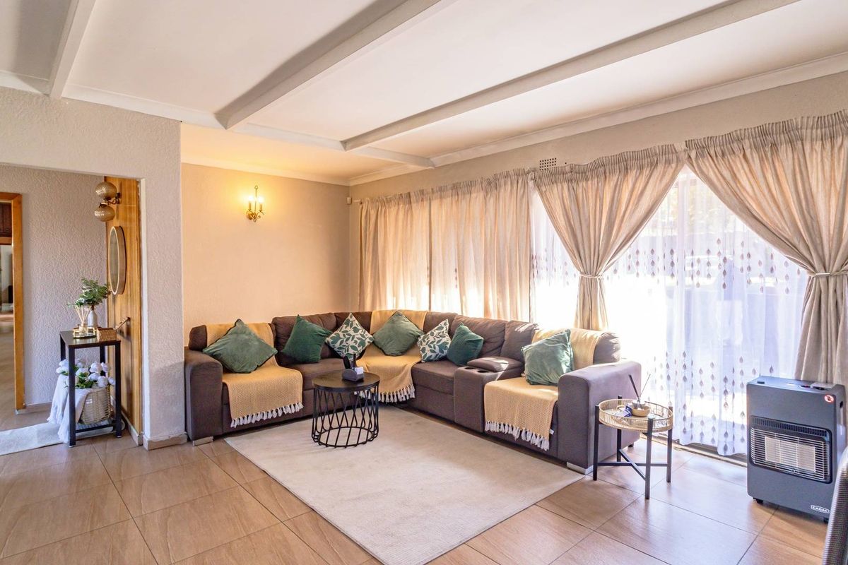 A spacious living room featuring tiled flooring, exposed ceiling beams, and large sliding glass doors that provide ample natural light.