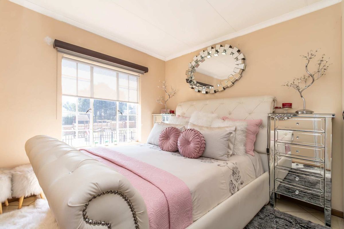 A well-lit bedroom featuring neutral wall tones, tiled flooring, and a large window with a roller blind.