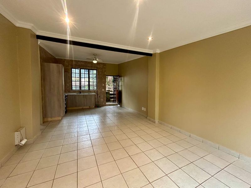 An open-plan living and kitchen area featuring tiled flooring, recessed lighting, and functional cabinetry, offering a blank canvas for potential interior updates.
