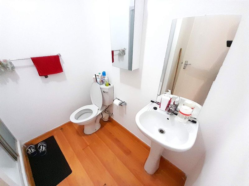 A functional bathroom featuring a pedestal washbasin, toilet, wall-mounted medicine cabinet, and mirror, finished with wood-look flooring.