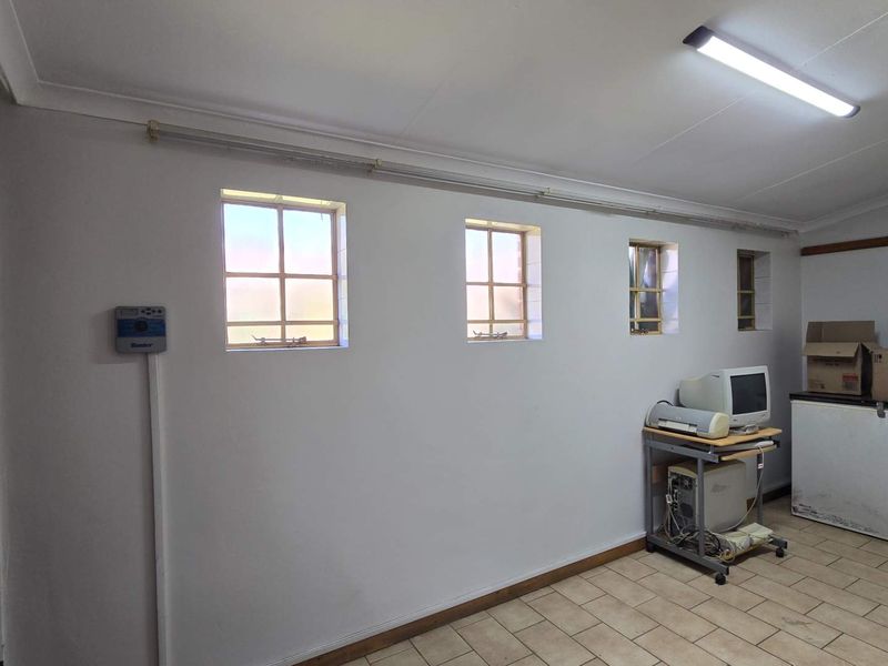 A functional utility space featuring tiled flooring, multiple small windows, and a security gate, suitable for storage or a home office setup.