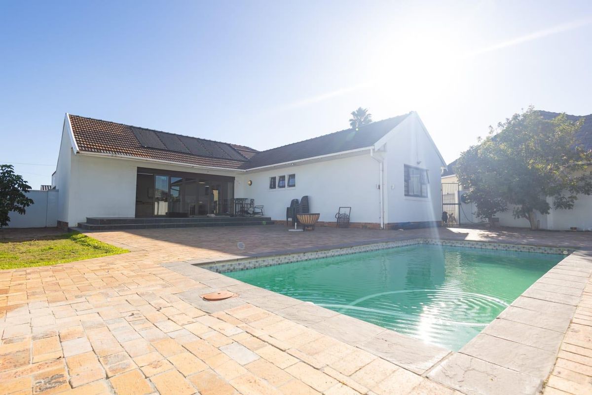 Rear exterior view of the house featuring a swimming pool, paved patio area, and solar panels installed on the tiled roof.