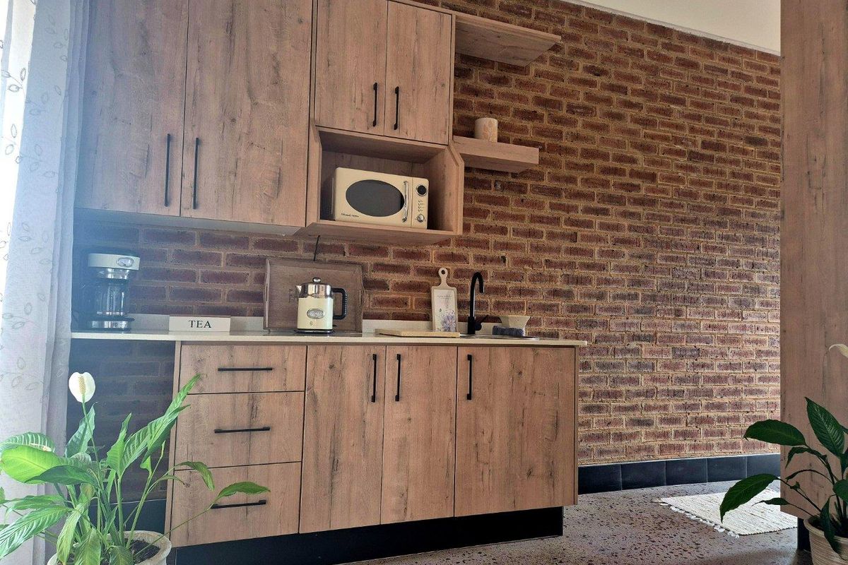 A modern kitchen area featuring wood-look cabinetry, a built-in microwave, stone countertops, and a striking exposed brick wall with terrazzo flooring.