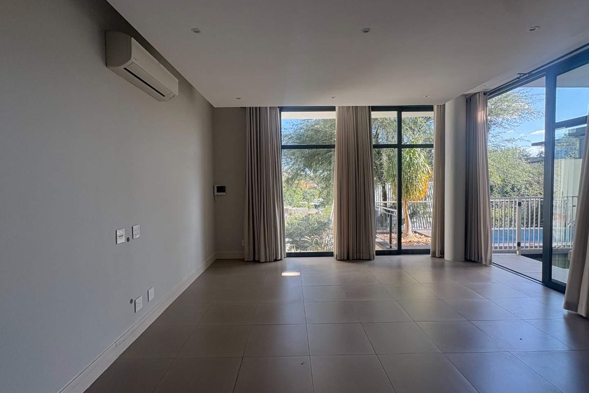 Spacious open-plan living area featuring large floor-to-ceiling windows, tiled flooring, and a wall-mounted air conditioning unit, with direct access to an outdoor patio.
