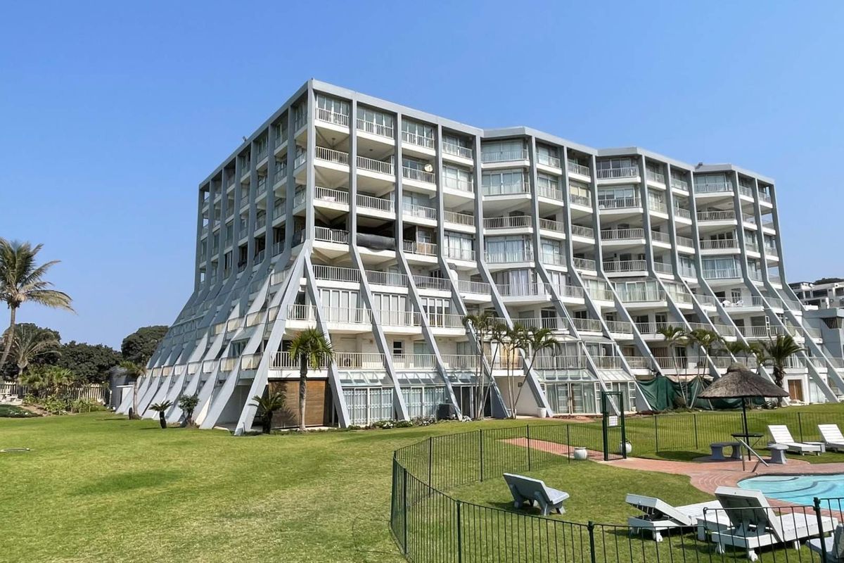 Rear view of a multi-story apartment building featuring distinctive concrete structural buttresses, private balconies, and access to a communal swimming pool and garden area.