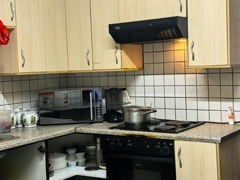 Compact kitchen featuring light wood-finish cabinetry, granite countertops, a built-in oven with hob, and a tiled backsplash.