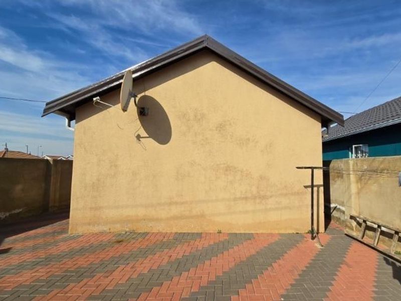 Rear exterior view of the property featuring a paved courtyard, boundary walls, and a satellite dish mounted on the side wall.