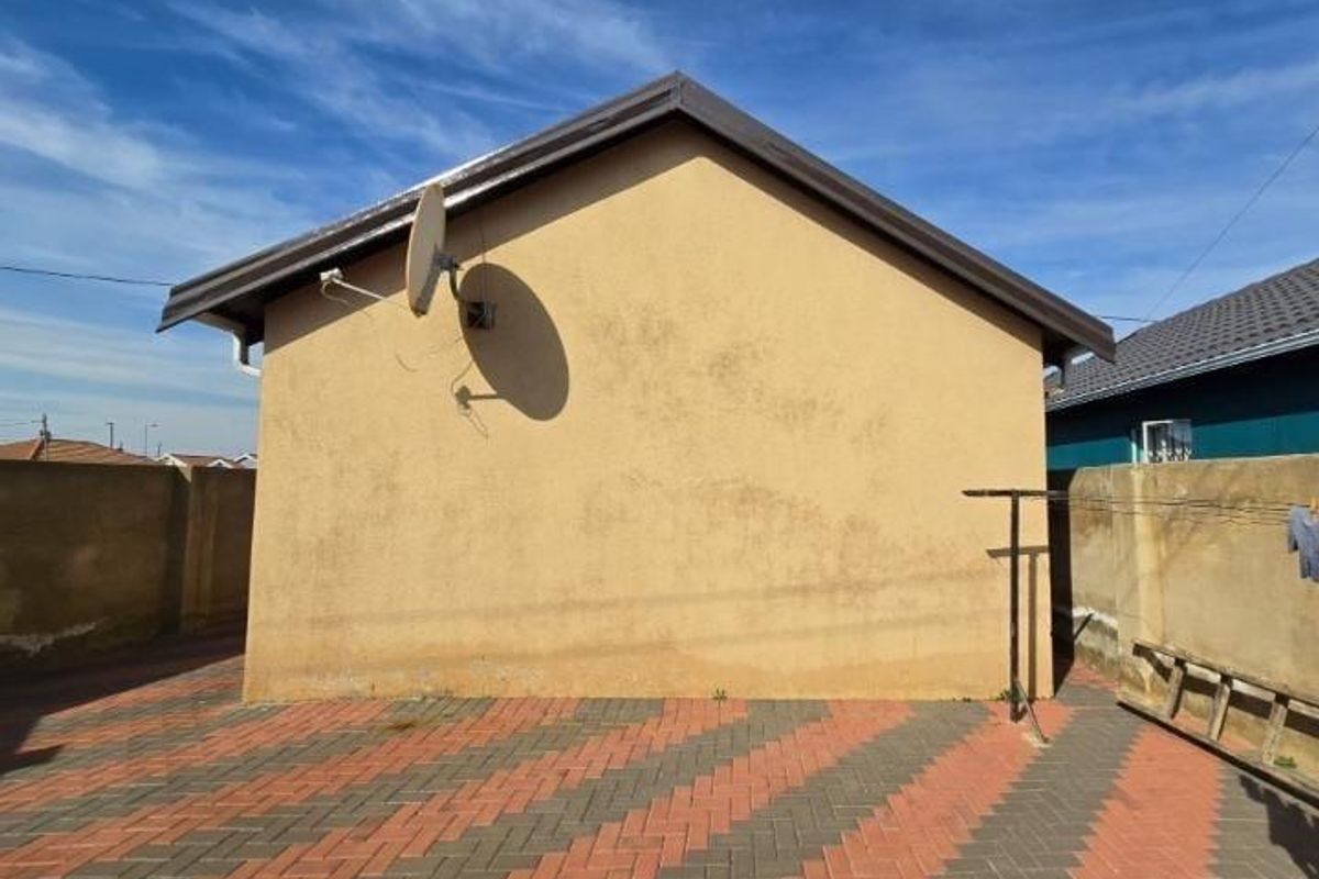 Rear exterior view of the property featuring a paved courtyard, boundary walls, and a satellite dish mounted on the side wall.
