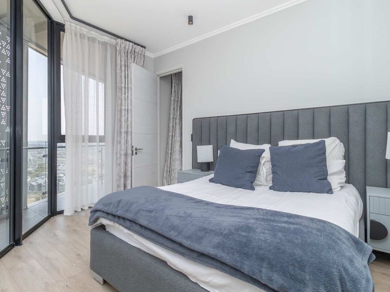 Modern bedroom featuring light laminate flooring, floor-to-ceiling glass doors leading to a balcony, and a decorative exterior privacy screen.