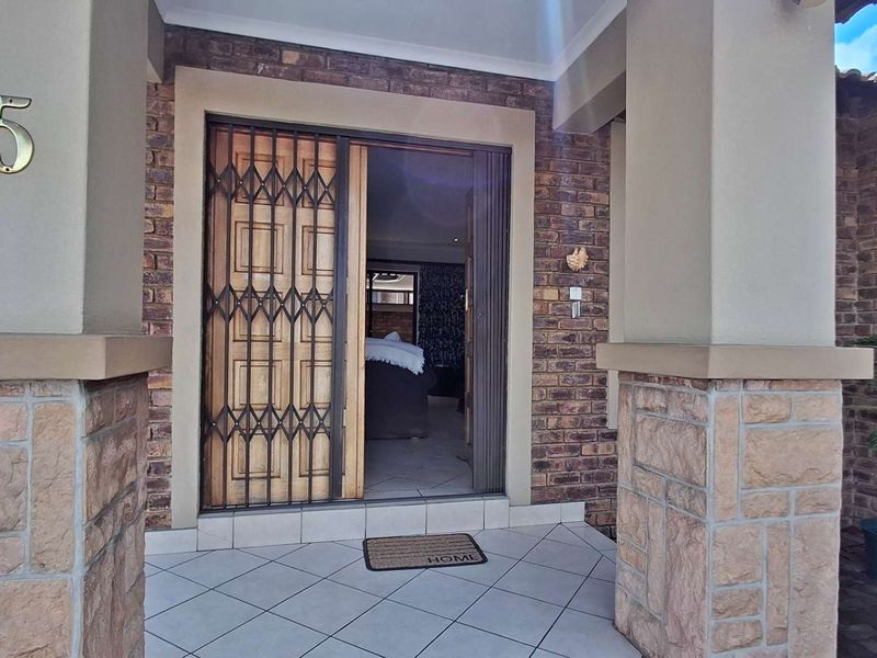 Front entrance of the townhouse featuring a tiled porch, brick and stone facade, and a secure metal gate.
