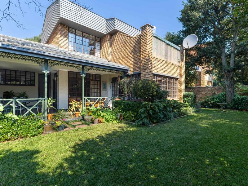 Rear view of a townhouse featuring a brick facade, a covered patio with decorative ironwork, and a well-maintained garden.