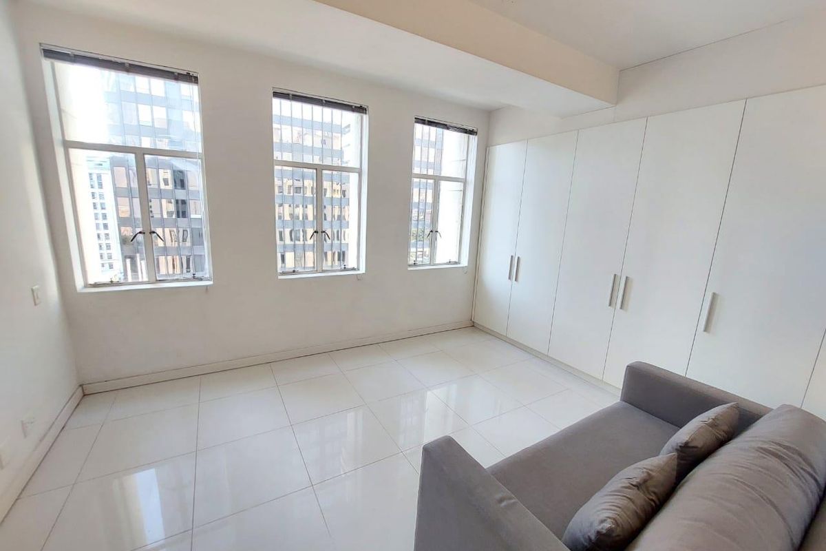 Bright bedroom featuring large windows with security bars, polished tiled flooring, and extensive built-in wardrobe storage.