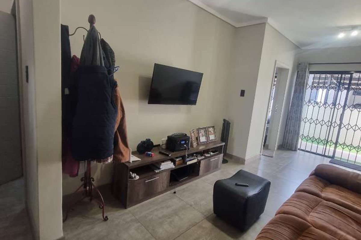 A living room featuring large format floor tiles, neutral wall tones, and a security gate leading to an outdoor area.