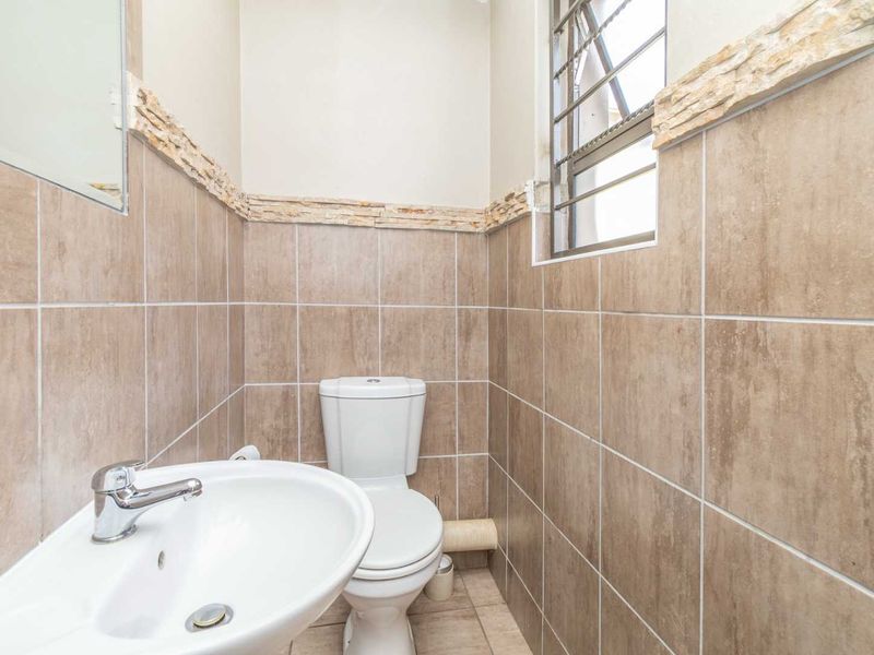 A compact, tiled bathroom featuring a pedestal basin, chrome mixer tap, and a standard toilet with a window for natural light.