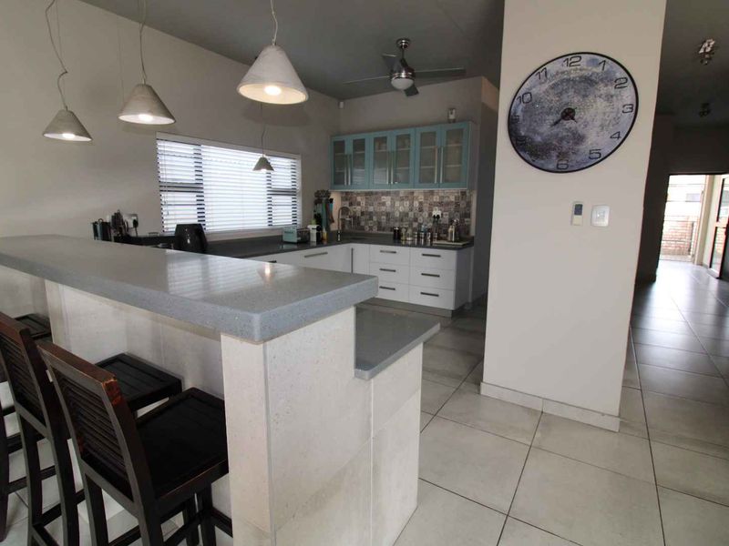 Modern kitchen featuring a breakfast bar with stone countertops, ample cabinetry, tiled backsplash, and pendant lighting, seamlessly integrated into the living space.