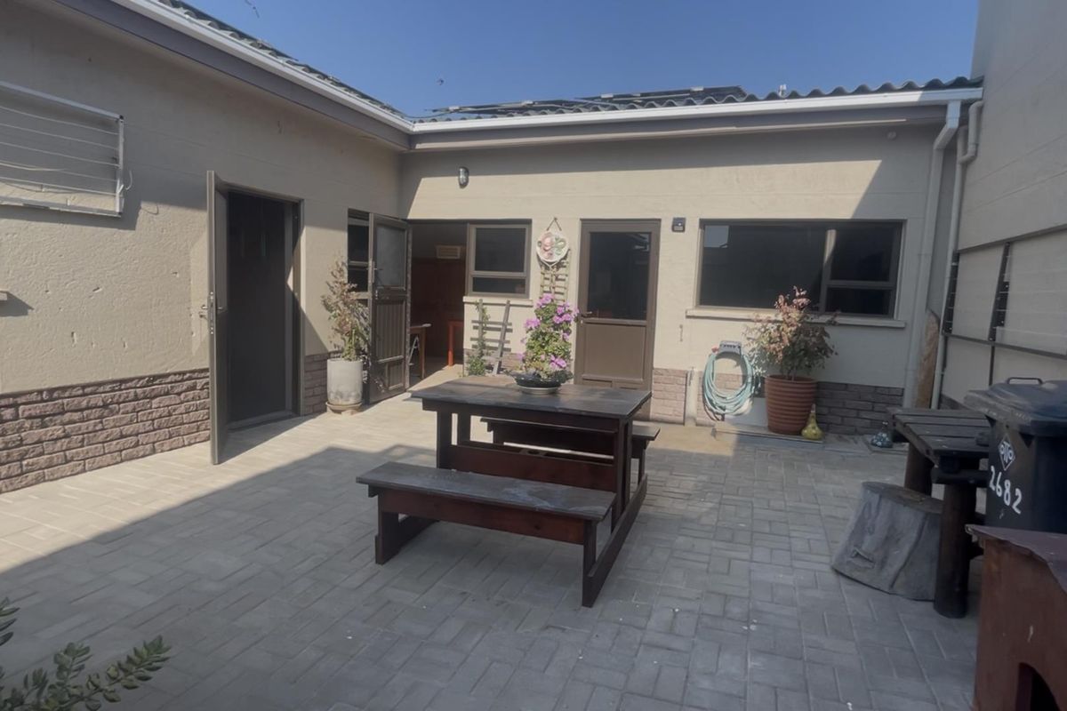 A paved rear courtyard area featuring brick base detailing, aluminium window frames, and direct access to the home's interior living spaces.
